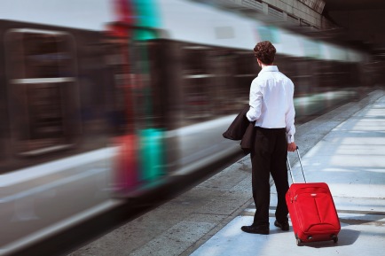 man-with-suitcase-on-railway-platform watching commuter train